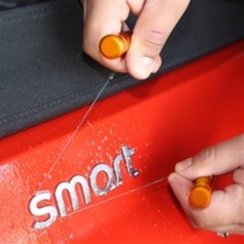 A person using the car emblem removal tool on a 'smart' car emblem, demonstrating the tool's use.