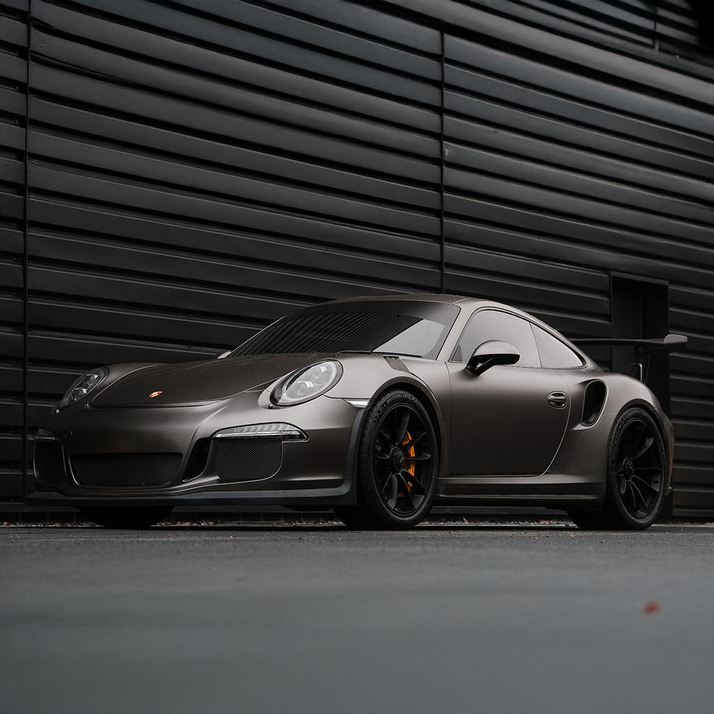 Gray sports car parked in front of a black, slatted wall.