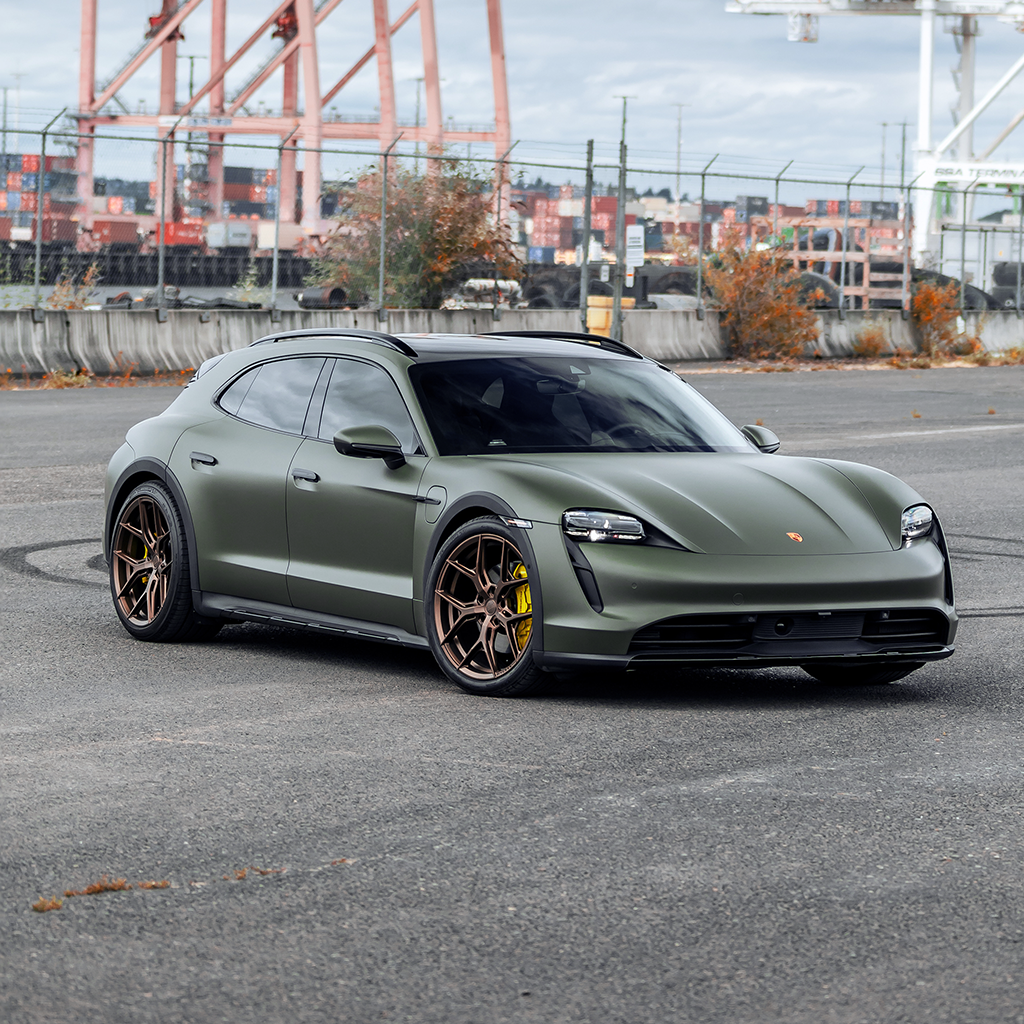 Green Porsche SUV parked on a concrete surface with industrial background