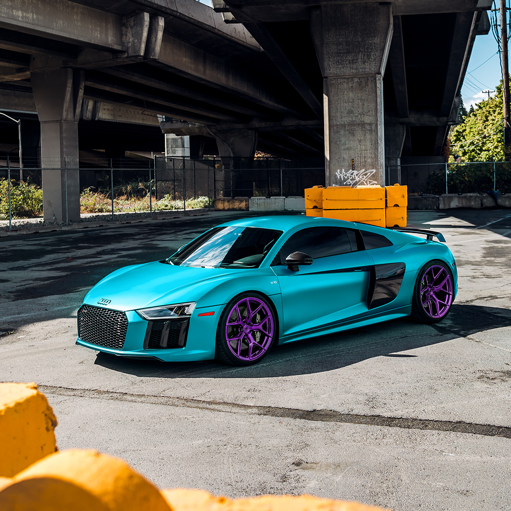 Turquoise Audi sports car with purple rims parked under a bridge.