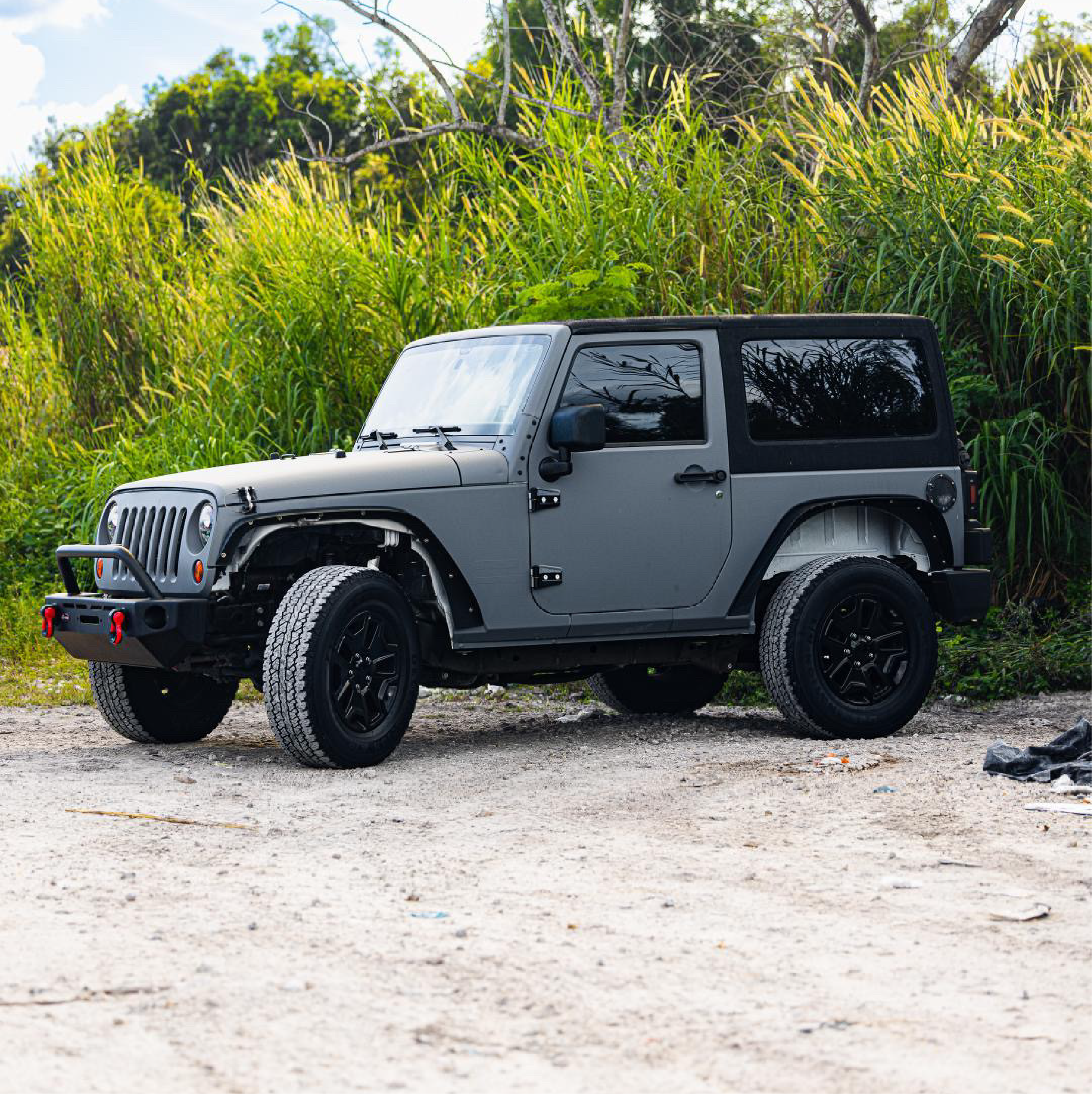 Nardo grey Jeep SUV with custom black car wrap featuring a bird design, parked on asphalt with a background of trees.