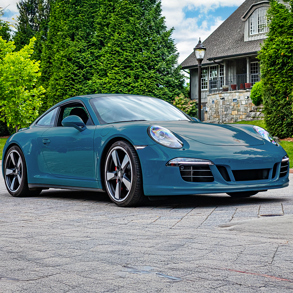 Blue sports car parked on a driveway with a house and trees in the background