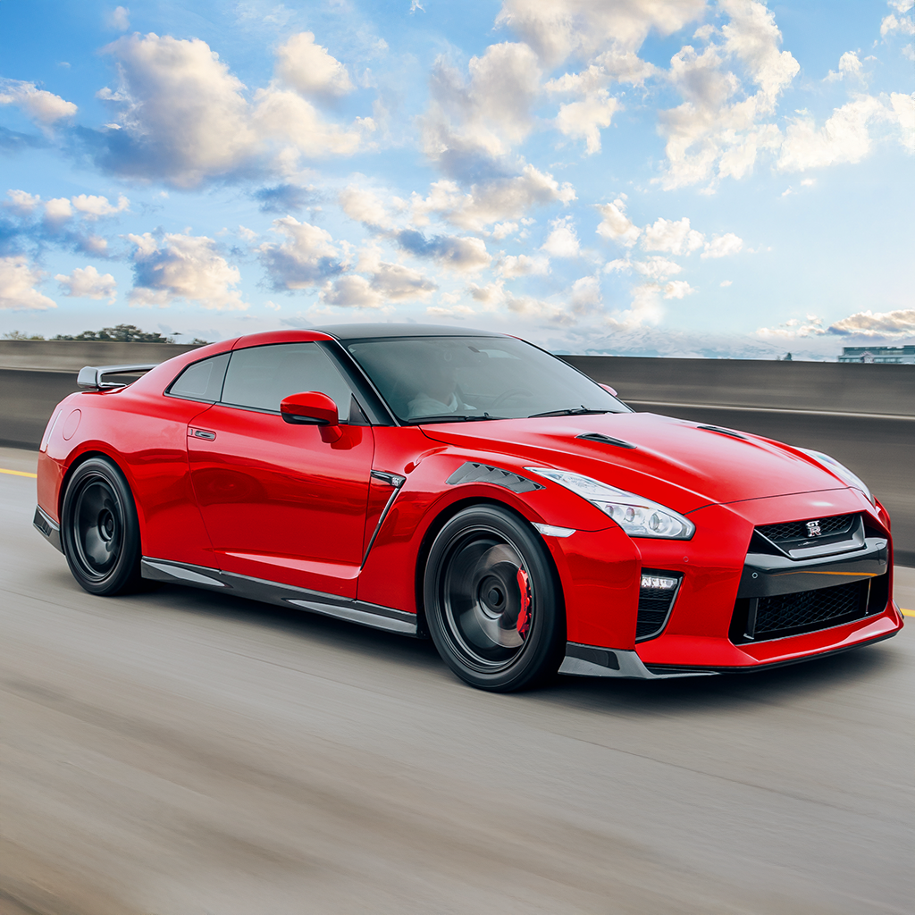 Red sports car on a track with a blue sky and clouds in the background