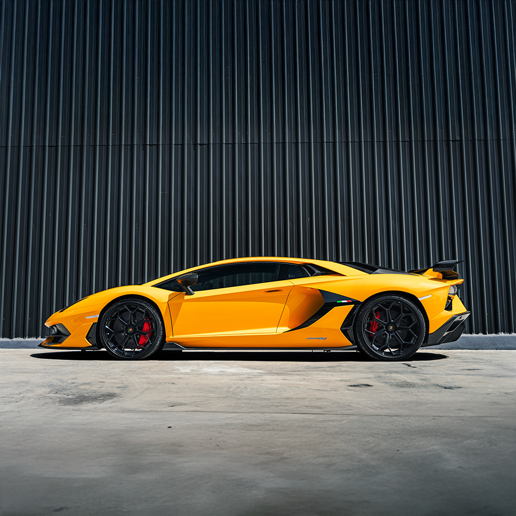 Yellow sports car parked in front of a dark vertical panel wall