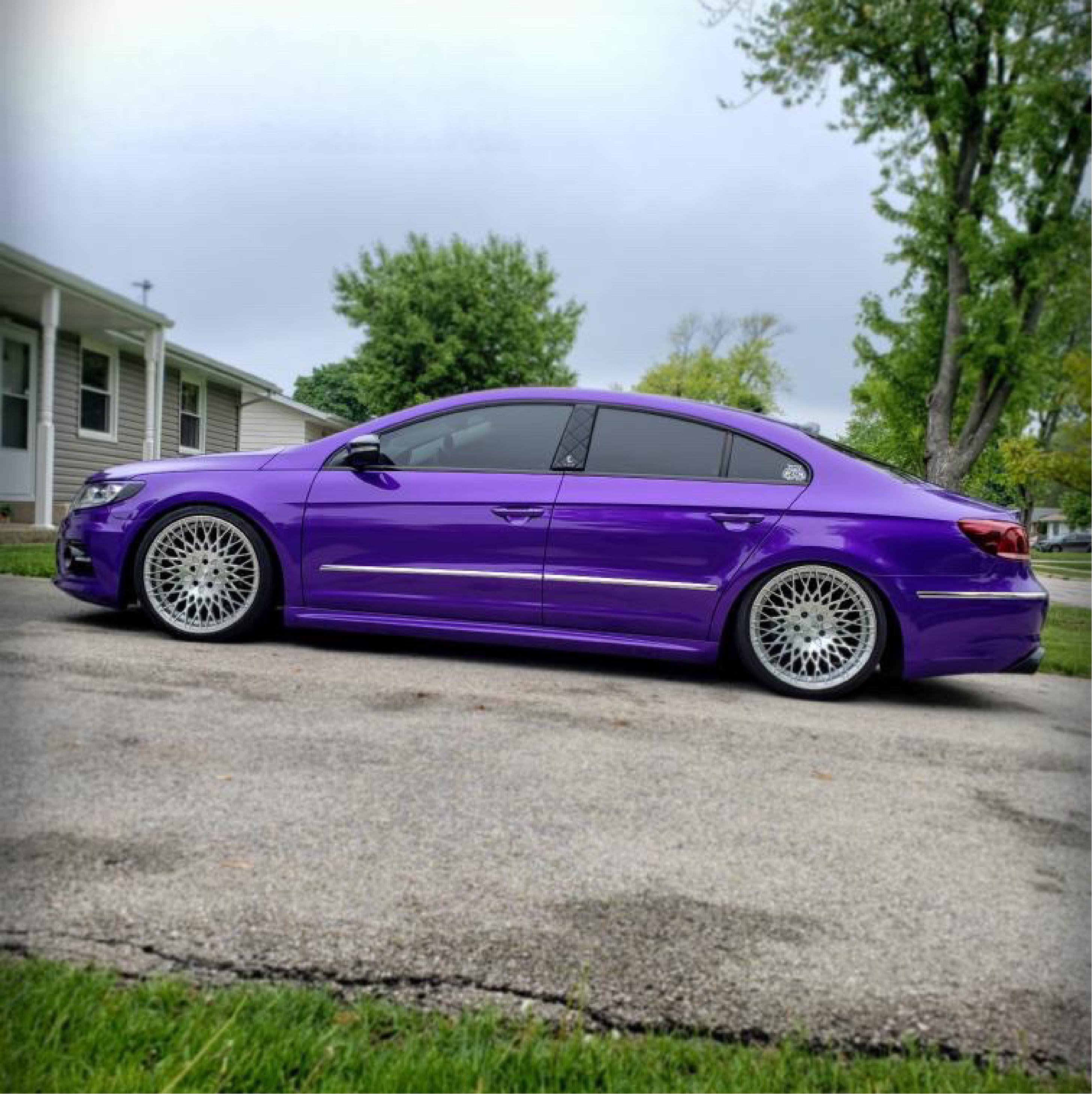 Purple car parked on a driveway with a house and trees in the background