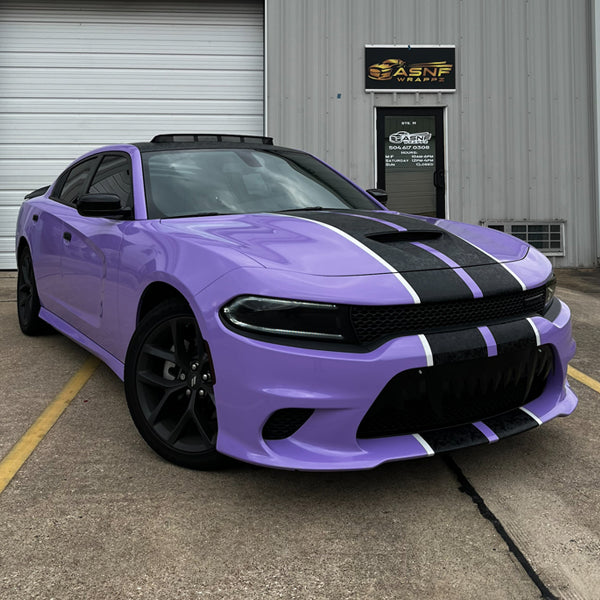 Front three-quarter view of a Dodge Charger showcasing a vibrant pearl gloss lavender vinyl wrap, accented with black and white racing stripes on the hood and bumper.