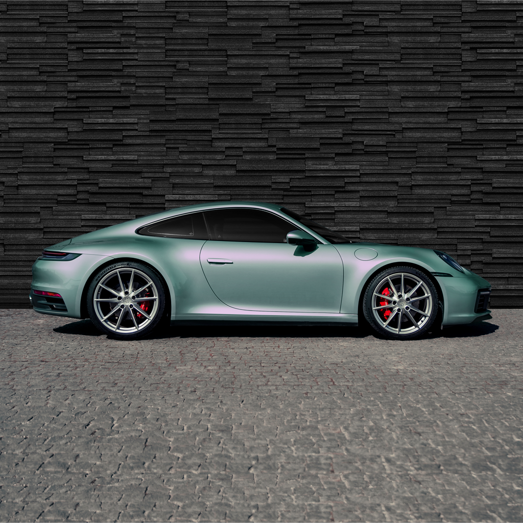 Green sports car parked on a textured surface with a dark brick wall background