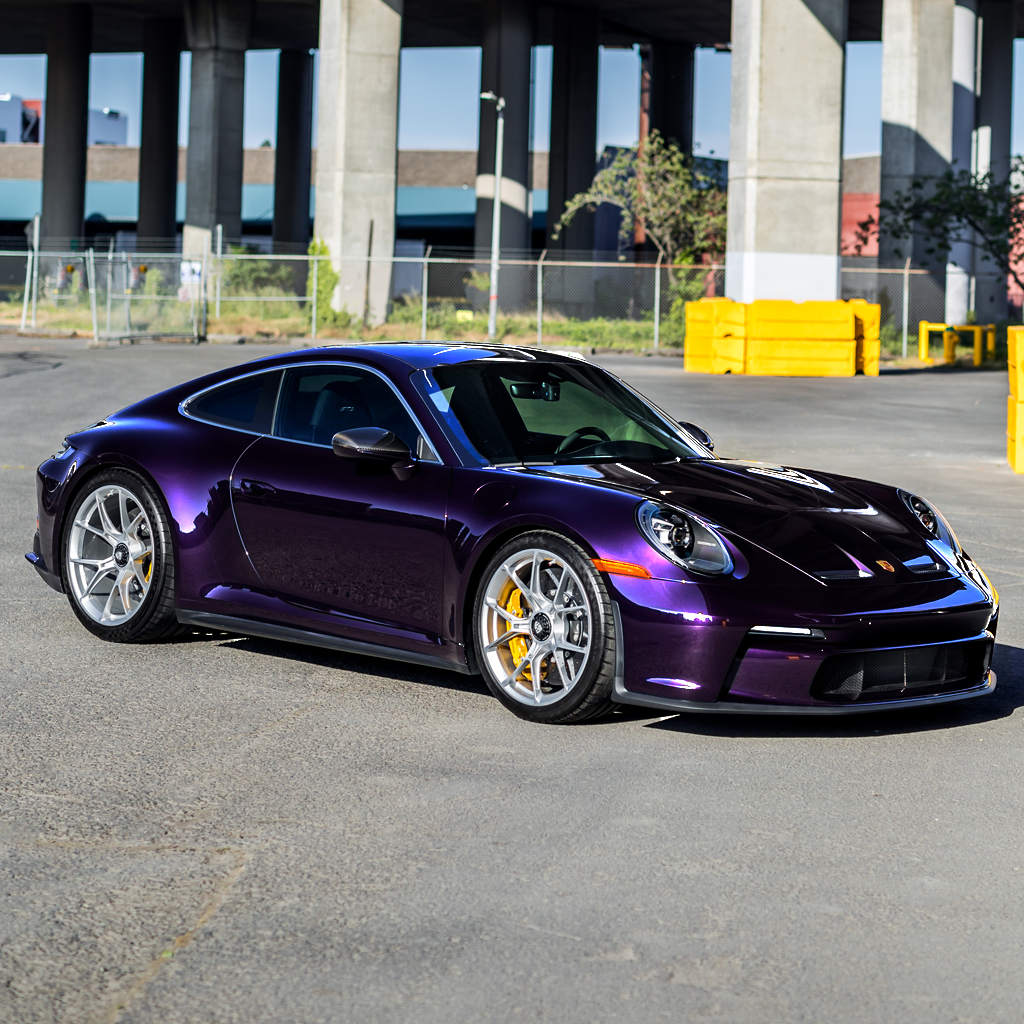 Purple sports car parked on a road with a bridge in the background