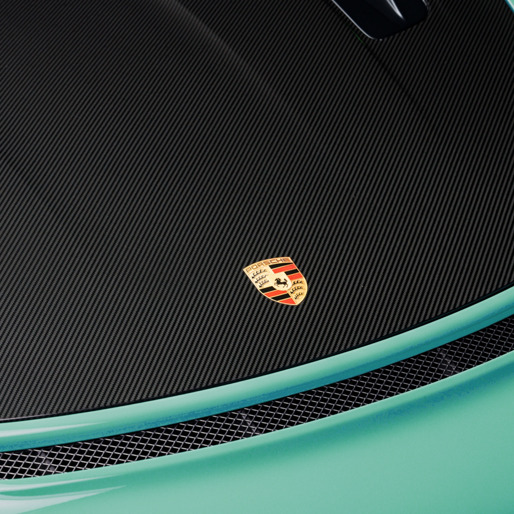 Close-up of a Porsche emblem on a car's carbon fiber surface.
