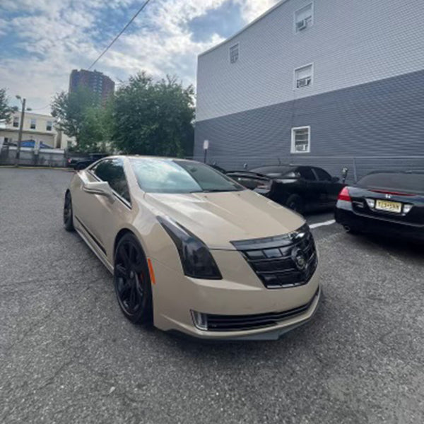 Cadillac ELR with gloss desert tan vinyl wrap and blacked-out trim, parked outdoors in a city lot under a partly cloudy sky.