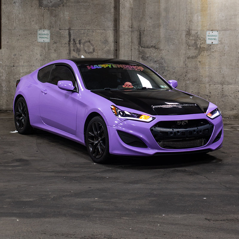 A static shot of a custom Hyundai Genesis Coupe featuring a gloss pearl lavender vinyl wrap and a vented carbon fiber hood, parked in a concrete garage.