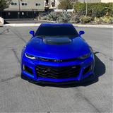 Blue Chevrolet car parked on a street with buildings and plants in the background