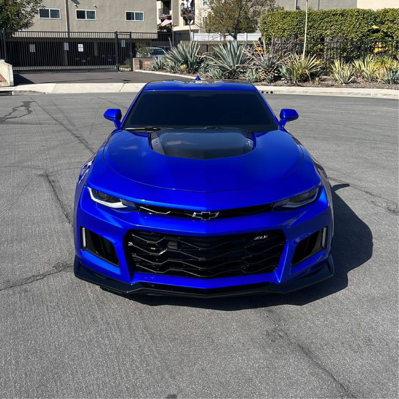 Blue Chevrolet car parked on a street with buildings and plants in the background