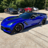 Blue sports car parked on a gravel surface with other cars in the background.