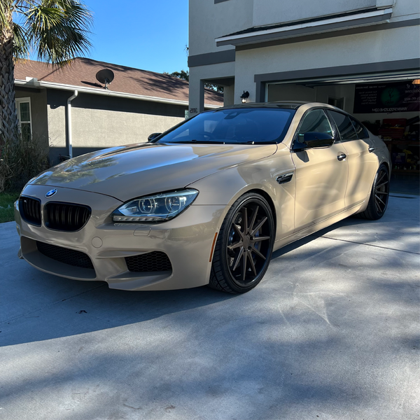BMW sedan wrapped in gloss desert tan car wrap with black accents, parked in a residential driveway.