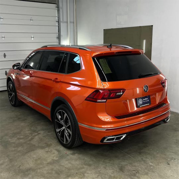 Rear three-quarter view of a Volkswagen Tiguan after being wrapped in a gloss lava orange metallic vinyl, highlighting the seamless application on the tailgate and bumper.