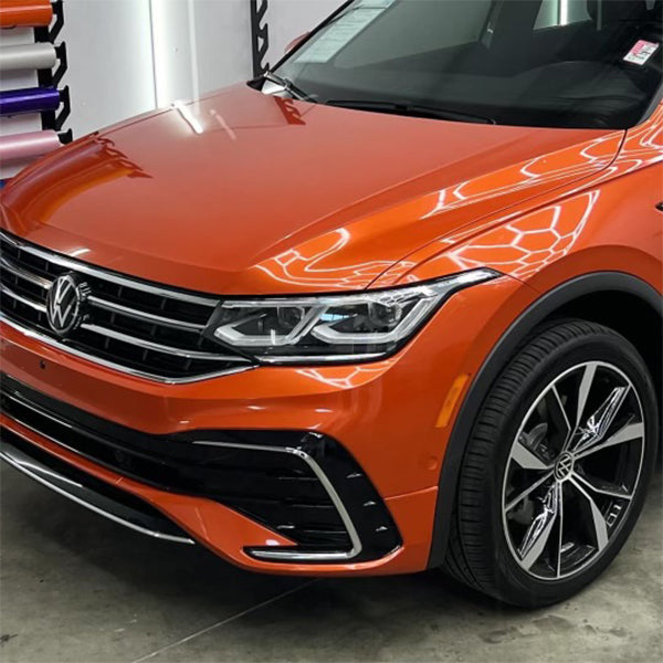 Front driver side view of a Volkswagen SUV showcasing a new gloss lava orange metallic vinyl car wrap in a detailing shop