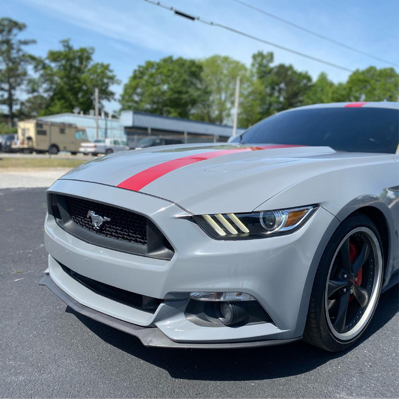 Gray Ford Mustang with a red stripe on a road with trees in the background