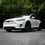 White Tesla Model X parked on a road with greenery in the background