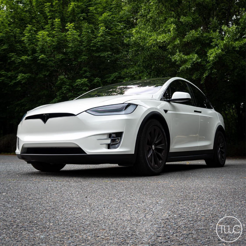 White Tesla Model X parked on a road with greenery in the background