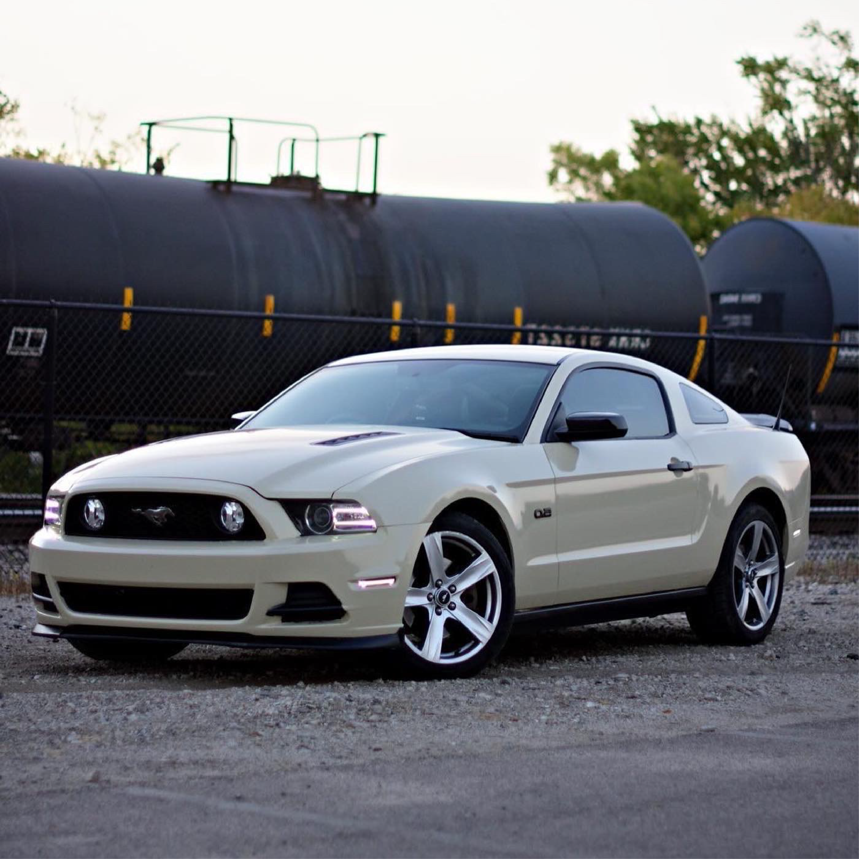 Beige Mustang car parked near a train with a clear sky background