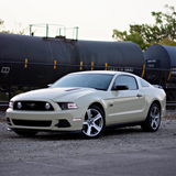 Beige Mustang car parked near a train with a clear sky background