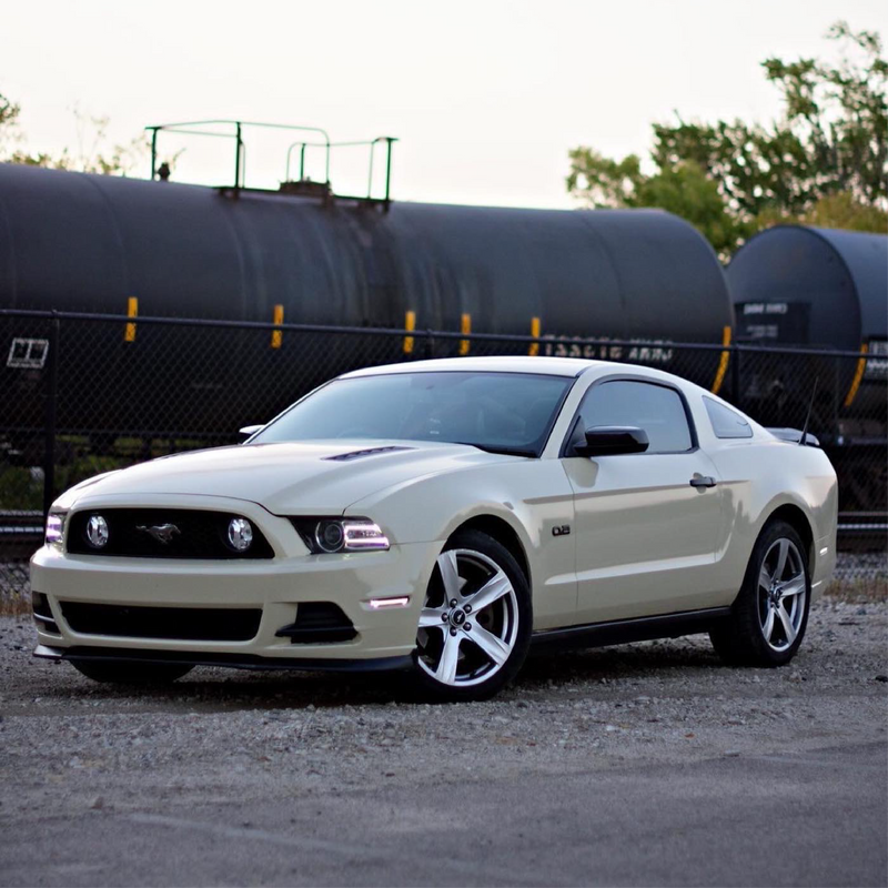 Beige Mustang car parked near a train with a clear sky background