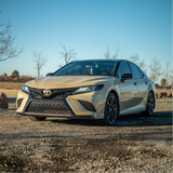 Beige Toyota car parked on a gravel surface with a clear blue sky.