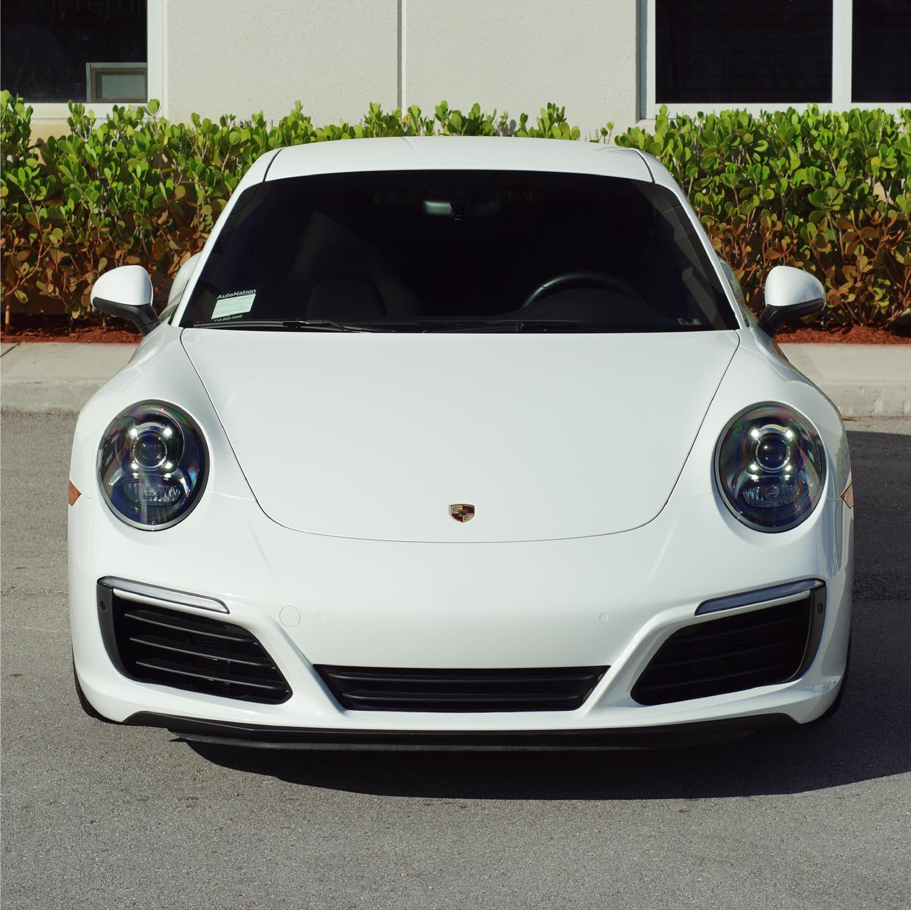 White Porsche car parked on a street with a building and greenery in the background