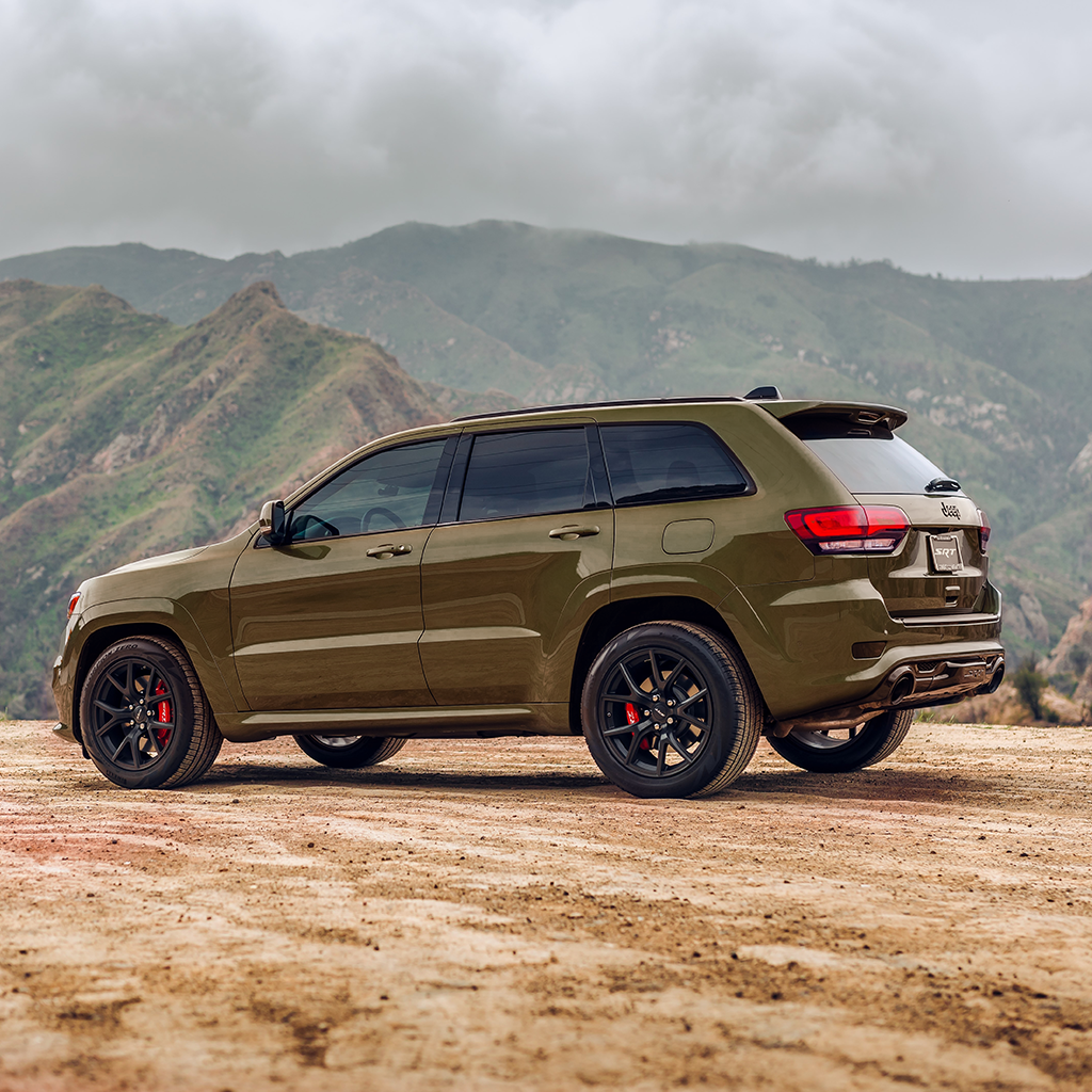 Green SUV on a dirt road with mountains in the background
