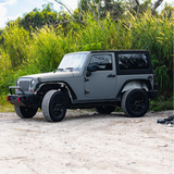 Nardo grey Jeep SUV with custom black car wrap featuring a bird design, parked on asphalt with a background of trees.