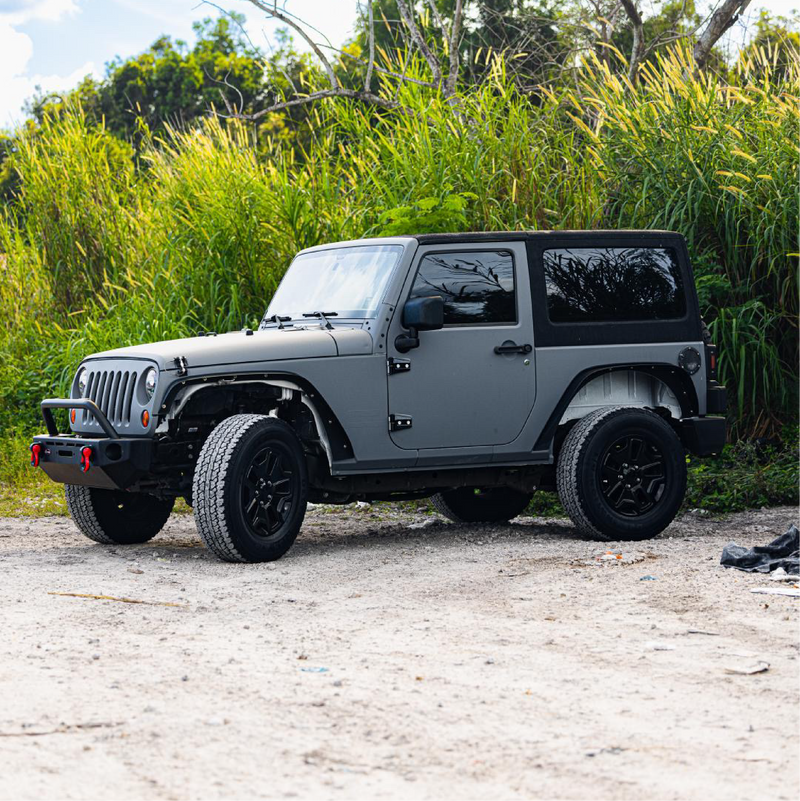Nardo grey Jeep SUV with custom black car wrap featuring a bird design, parked on asphalt with a background of trees.