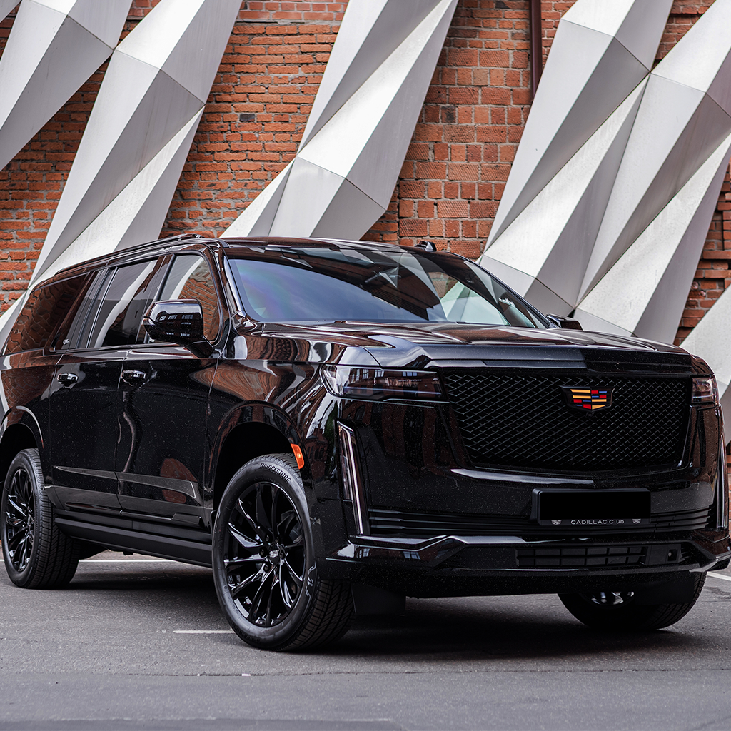 Black Cadillac SUV parked in front of a brick wall with geometric shapes.