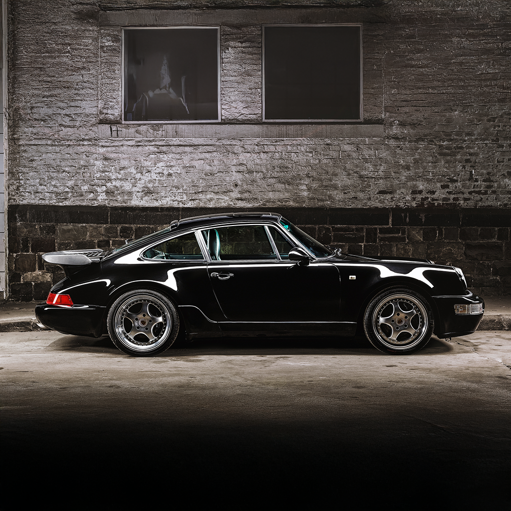Classic black Porsche 911 sports car parked in an industrial setting, showcasing its sleek curves, alloy wheels, and aerodynamic design.