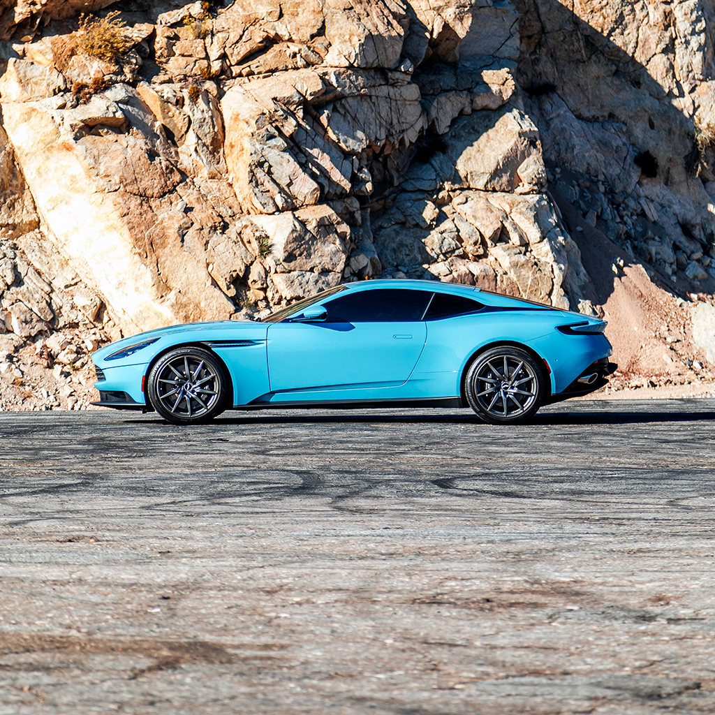 Blue sports car parked on a road with rocky cliffs in the background
