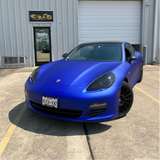 Blue Porsche parked in front of a building with a sign.
