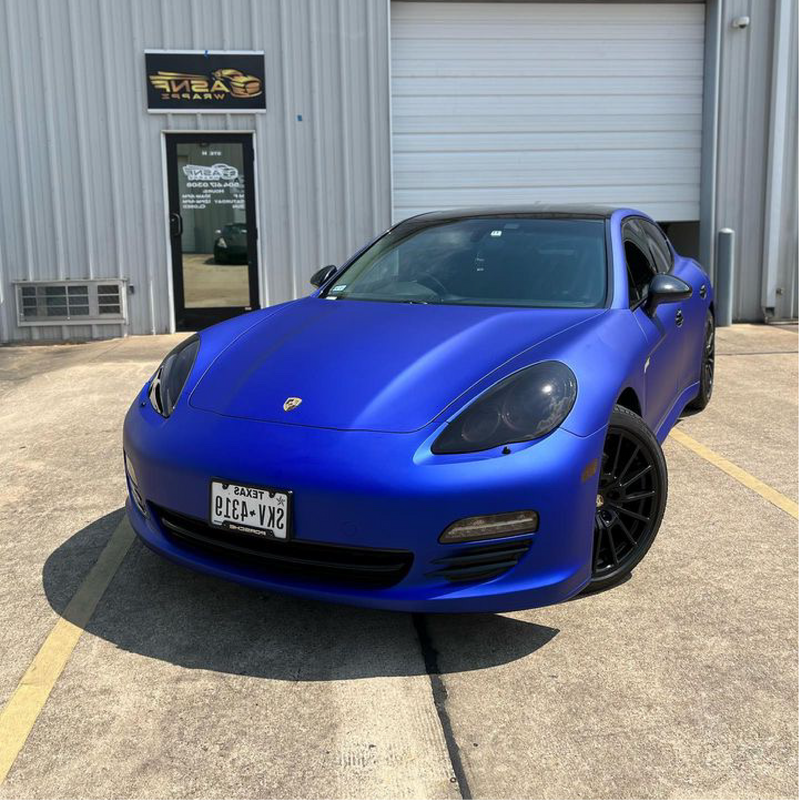Blue Porsche parked in front of a building with a sign.