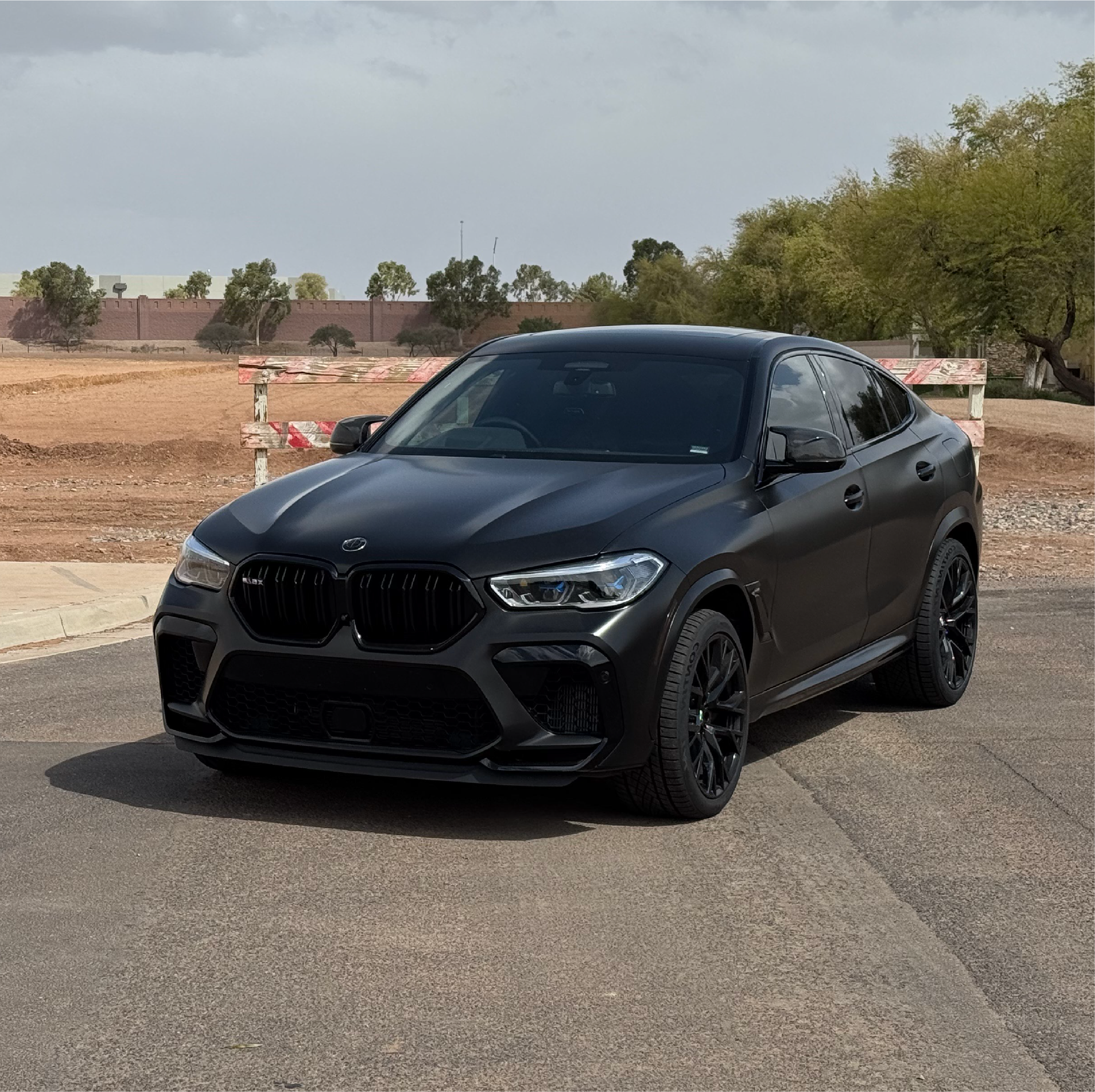 Black BMW SUV parked on a paved surface with trees and construction barriers in the background.