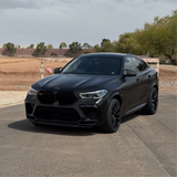 Black BMW SUV parked on a paved surface with trees and construction barriers in the background.