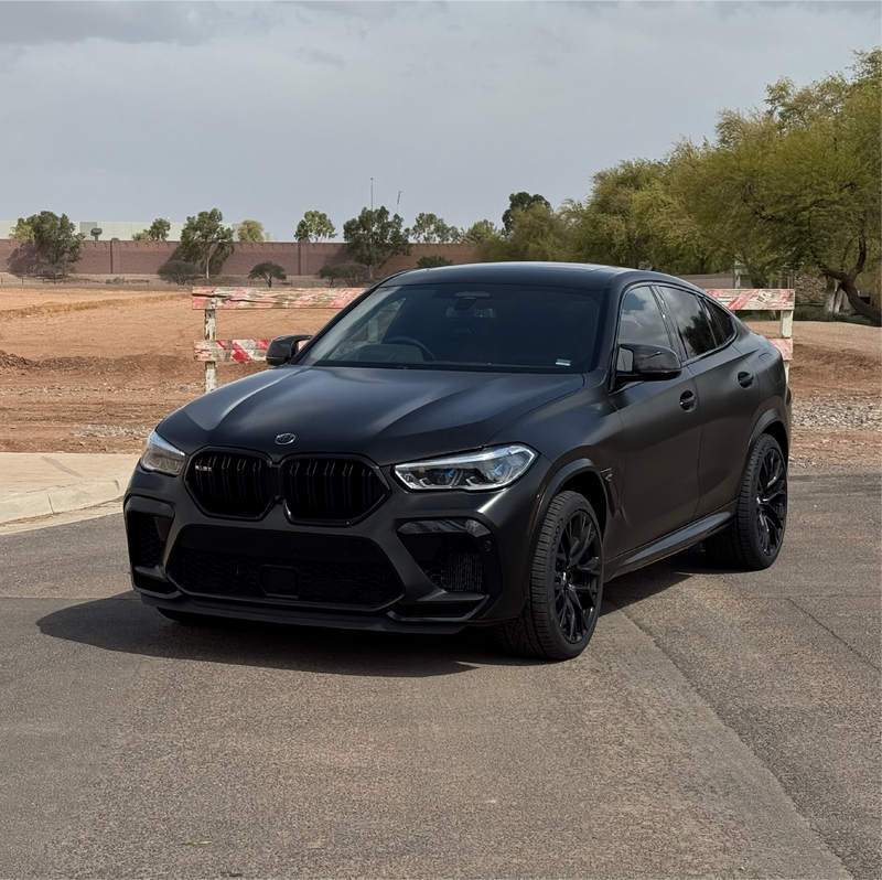 Black BMW SUV parked on a paved surface with trees and construction barriers in the background.
