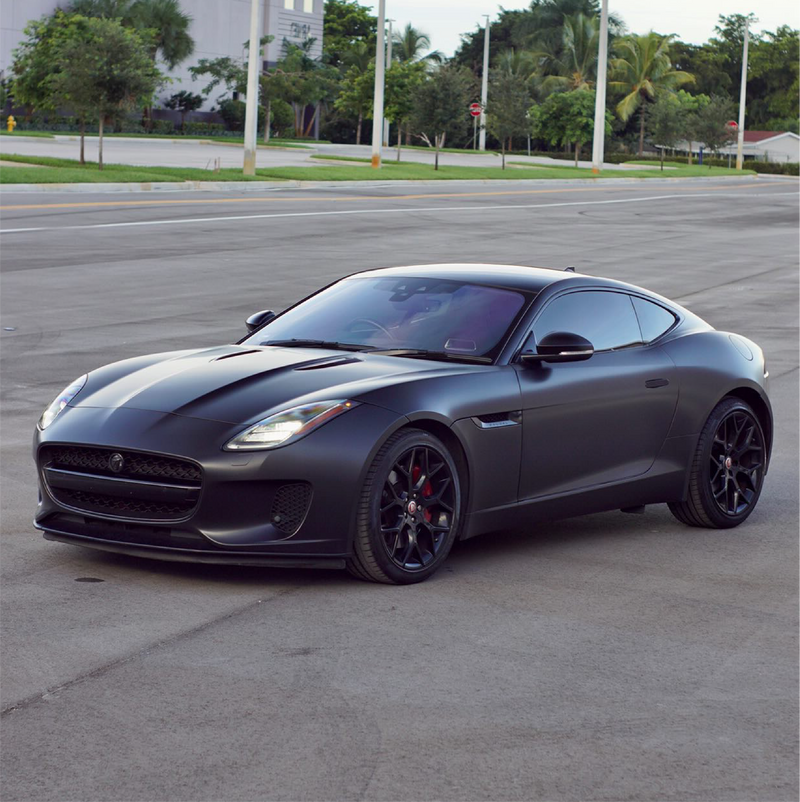 Black sports car on a city street with trees and buildings in the background