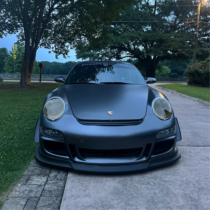 Black Porsche car parked on a driveway with trees in the background