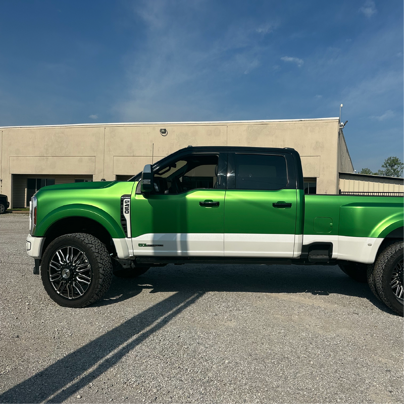 Green and white pickup truck parked on a concrete surface with a building in the background.