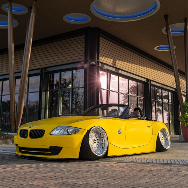 Yellow BMW convertible parked in front of a modern building with large windows.