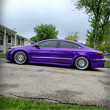 Purple car parked on a driveway with a house and trees in the background