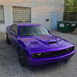 Purple muscle car parked in front of a building with a dumpster.