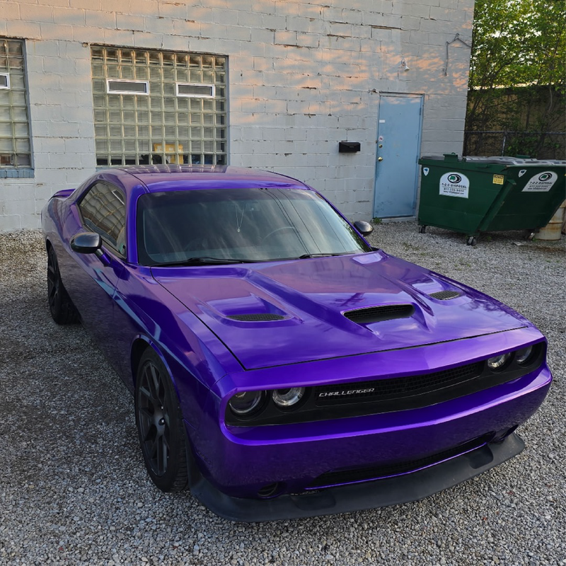 Purple muscle car parked in front of a building with a dumpster.