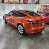 Orange Tesla Model 3 parked inside a building with graffiti on the wall.